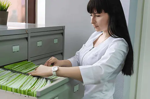 Records specialist pulling patient files from a medical records cabinet